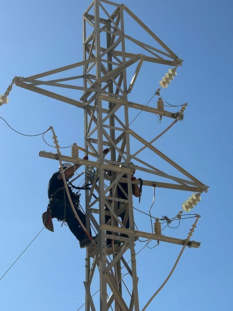 Técnicos electricistas realizando trabajos en torre de red eléctrica de alta tensión